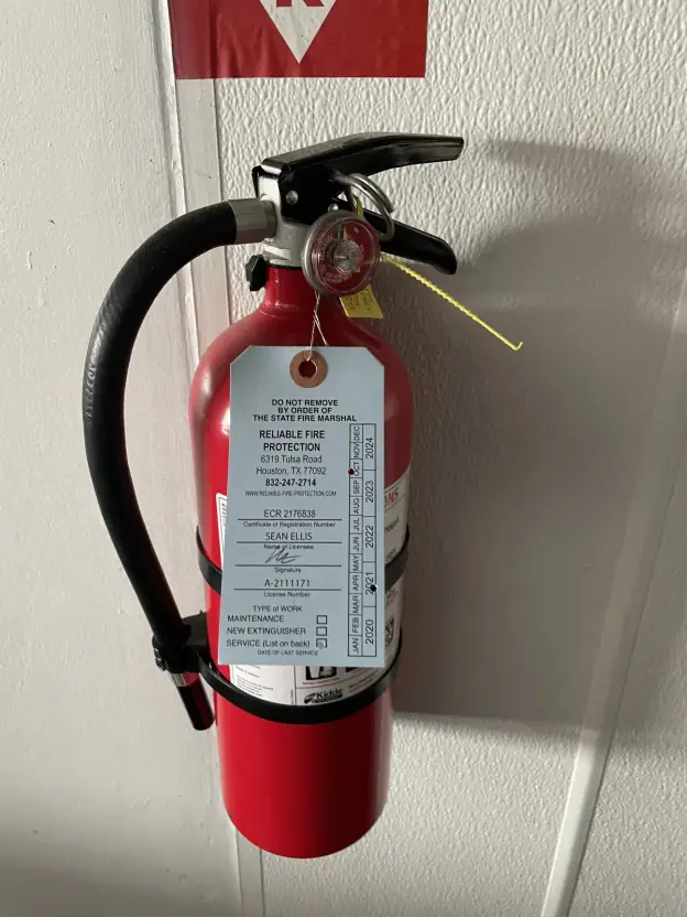 Reliable Fire Extinguisher Red fire extinguisher mounted on a wall with a maintenance tag from Reliable Fire Protection, emphasizing certified installation and inspection services for fire safety.