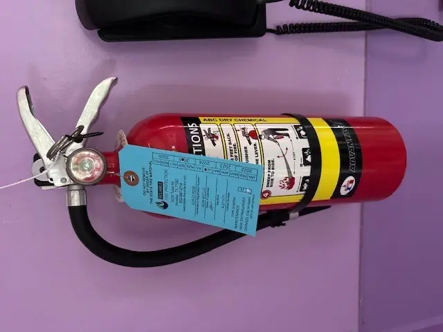 ABC dry chemical fire extinguisher mounted on a wall with its inspection tag