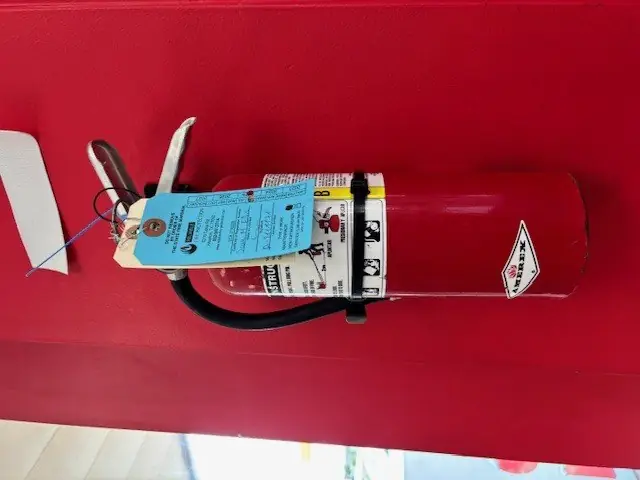 Amerex fire extinguisher on a red wall with an inspection tag