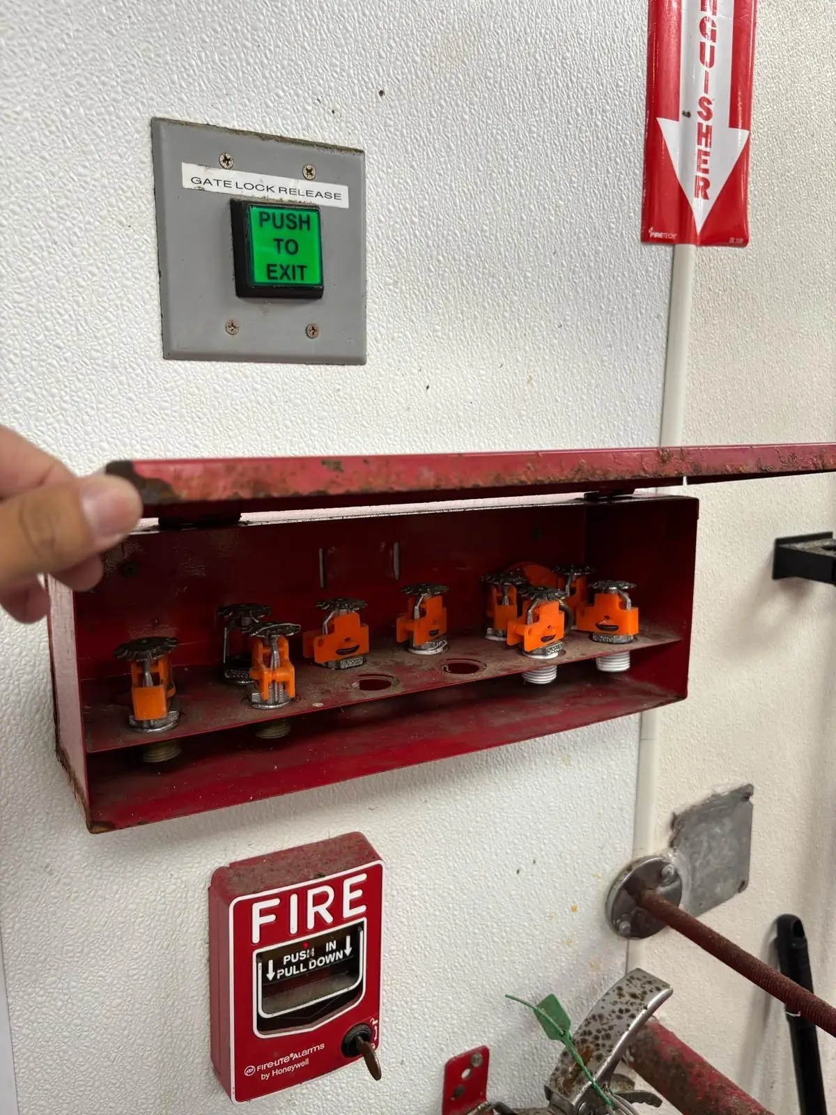 Spare sprinkler heads in an open cabinet beside a fire alarm pull station
