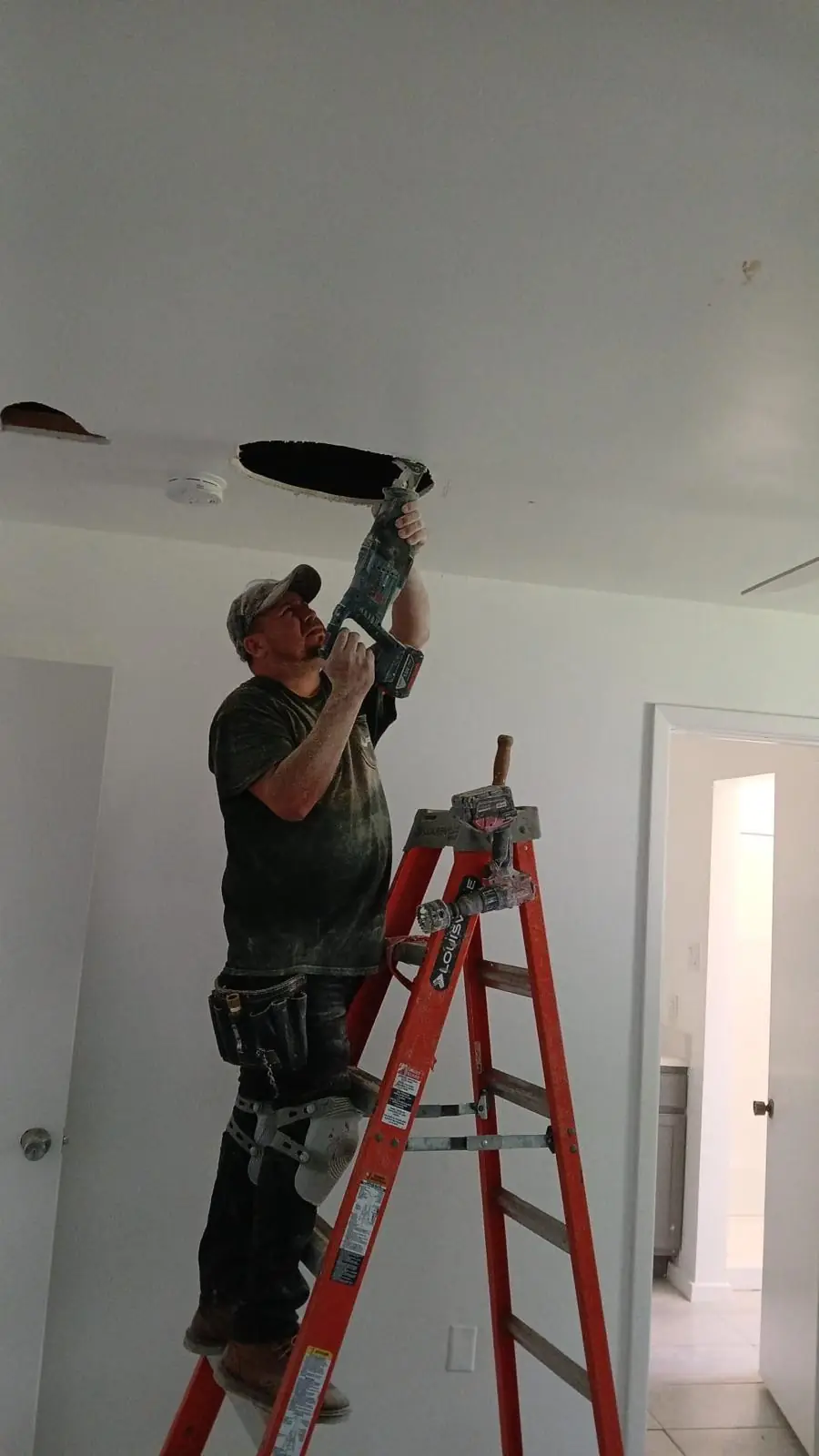 Technician on a ladder drilling the ceiling for a new sprinkler head