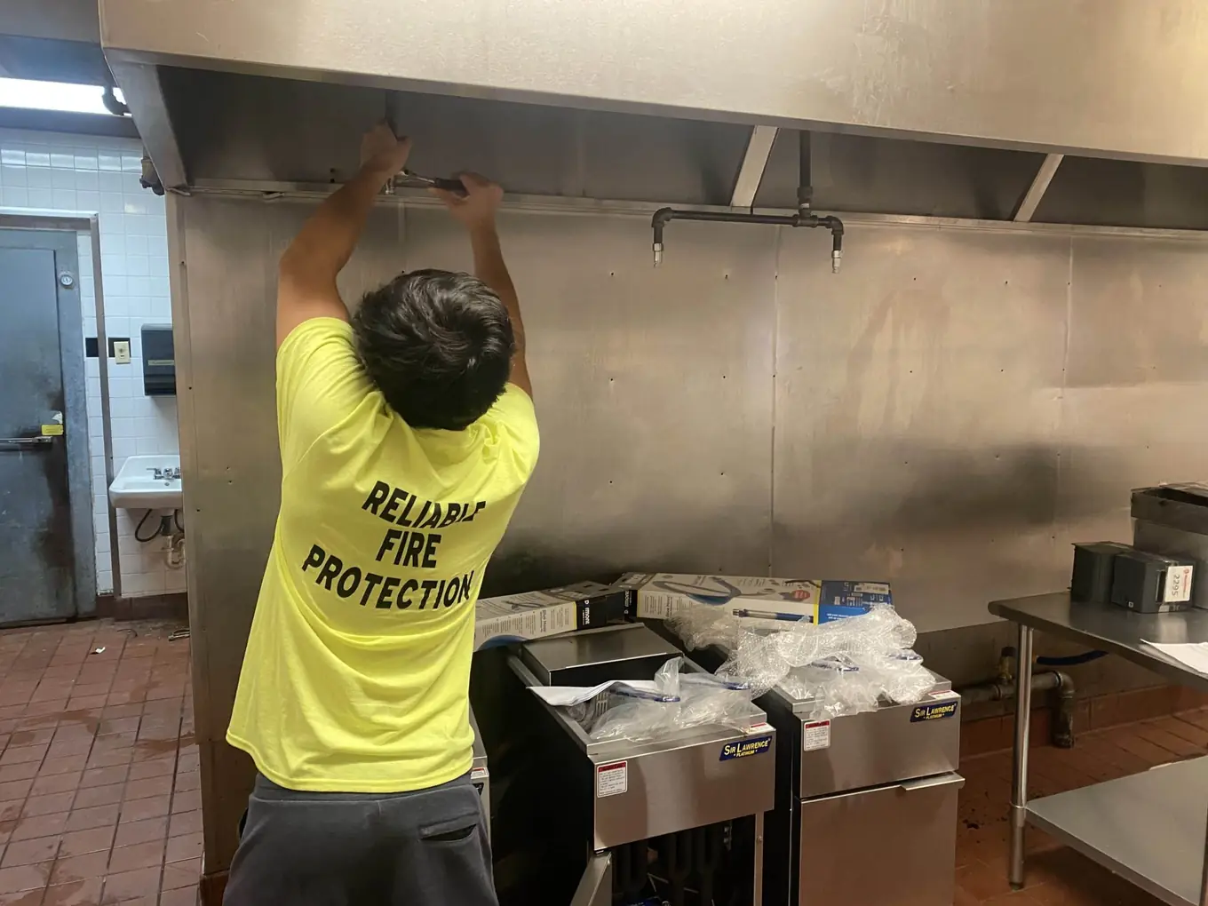 Technician in a Reliable Fire Protection shirt working under a commercial kitchen hood
