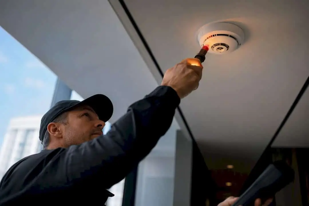 Technician testing a ceiling smoke detector with a test tool