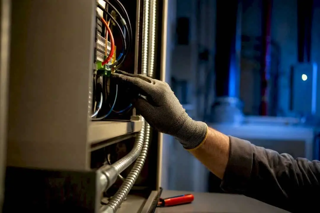 Gloved hand checking wiring connections in an alarm panel